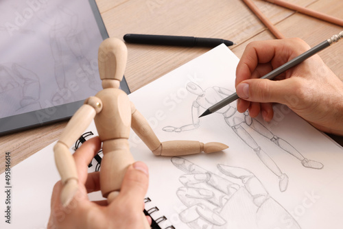 Man drawing mannequin in sketchbook with pencil at wooden table, closeup