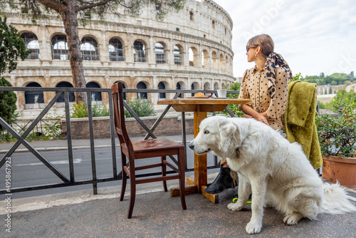 Woman sitting with her dog at outdoor cafe near coliseum, the most famous landmark in Rome. Concept of italian lifestyle with pets and traveling Italy