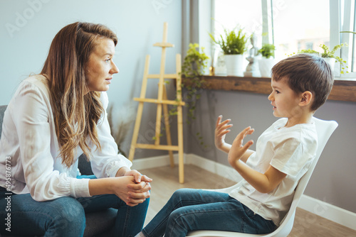 Young female psychologist working with little boy in office. Shot of a young child psychologist talking with a boy. Young female school psychologist having serious conversation with smart little boy