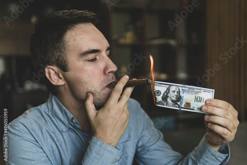 Young brutal businessman lighting cigar with 100 dollar bill as symbol of wealth and success. concept of wealth and extravagance.