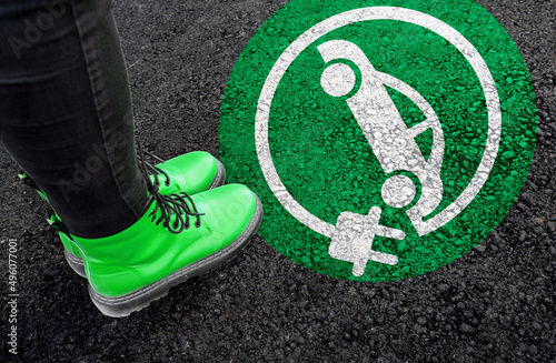 a woman with a boots is standing next to electric car sign on road asphalt 