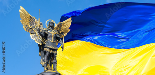 Statue of an angel on Independence Square in Kyiv. Archangel Michael is the heavenly patron of Kyiv. Large flag of ukraine in the background. Russian war in Ukraine.