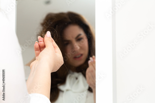 Young girl suffering from trichotillomania in the mirror looking at a lock of hair between her fingers