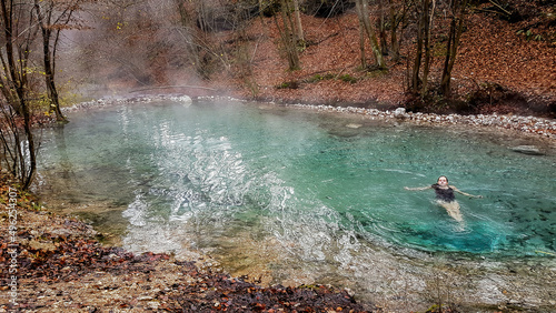 A girl in a black swimsuit swimming in a natural thermic spring in Maibachl, Austria during autumn. The thermic pool is located in the middle of the forest. Healing power of natural water. Relaxation