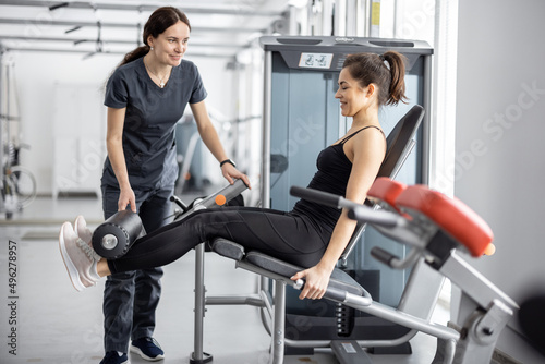 Woman doing exercises on simulator with rehabilitation specialist at the gym. Concept of physical therapy for strengthening and recovery. Idea of recovery after pregnancy