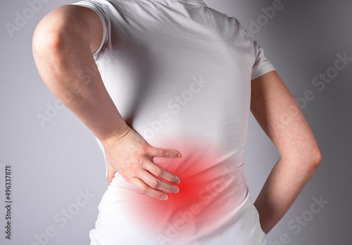 Backache. Woman suffering from lower back pain with red spot closeup. Muscle spasm, sprains, strains, inflammation. Sport, household injury, nervous diseases. Health care and medicine concept.