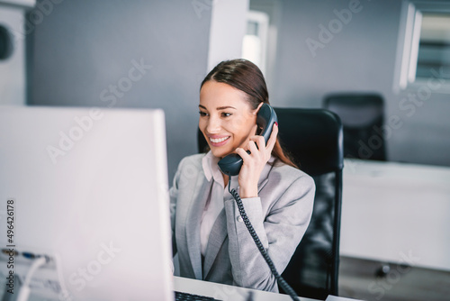 A friendly secretary answering phone call and using computer at office.