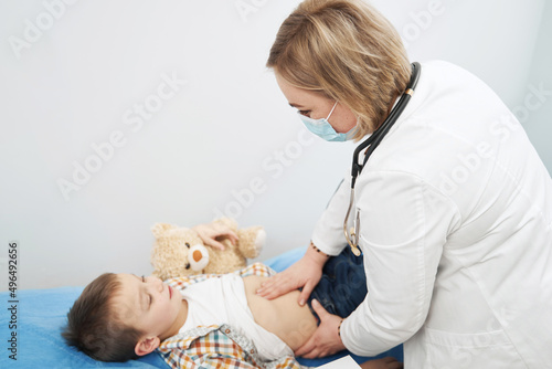 Female pediatrician examining child abdomen in clinic