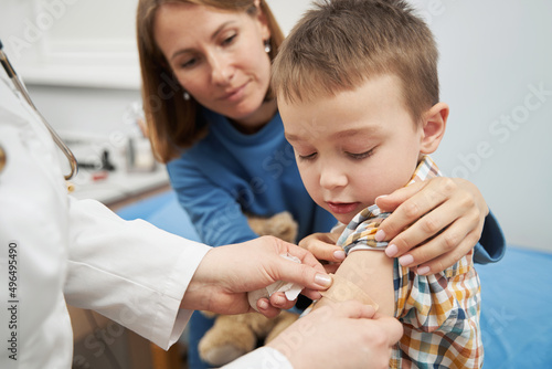 Doctor placing medical plaster on child arm after vaccination