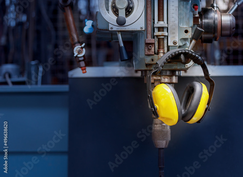 Yellow protective ear muffs hang on machines in heavy industrial plants.