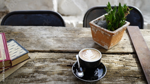 eine Tasse Cappuccino auf einem vintage Holztisch mit einer grünen Pflanze und Büchern