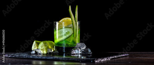 Cocktail with cucumber, ice on bar counter in a restaurant, pub. Fresh tonic drink with lime juice, mint, gin, cucumber juice. Alcoholic cooler beverage on black isolated background