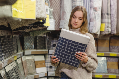 Young cheerful woman choosing cotton bedding set in home textile store show room