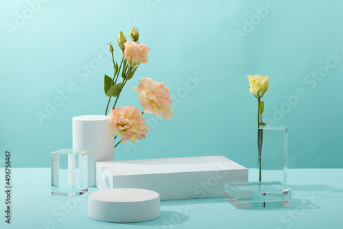 A front view of white and transparent podium decorated with flower and blue background with blank space for advertising 