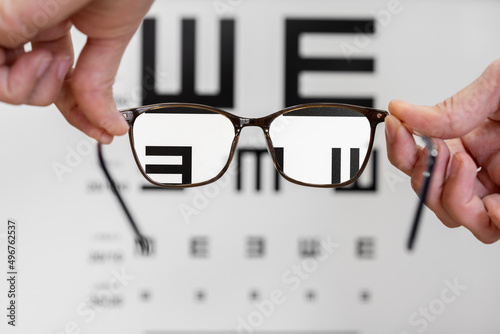 Optometric table with letter for check the vision. Hands holding a pair of glasses focusing on letters and blurred background