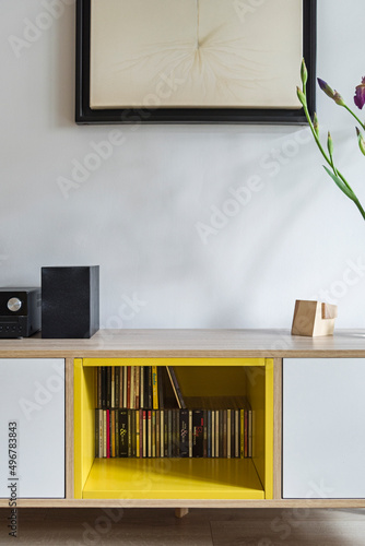Detal na przytulny salon z żółtymi akcentami kolorystycznymi. Półka z płytami CD
