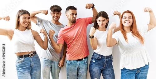 Group of young friends standing together over isolated background showing arms muscles smiling proud. fitness concept.
