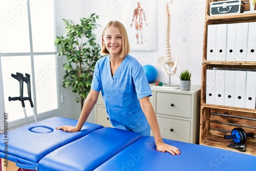 Young blonde woman wearing physiotherapist uniform standing at rehab clinic