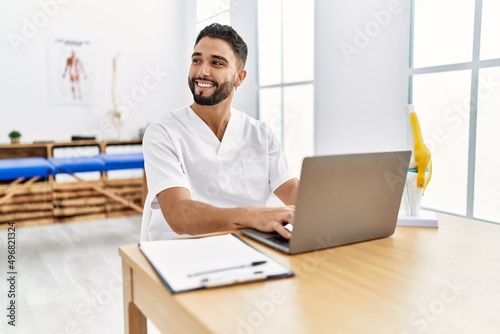 Young arab man wearing physiotherapist uniform using laptop at clinic