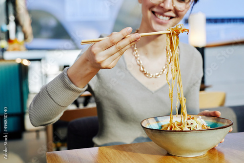 Close up of smiling young woman enjoying delicious Asian noodle in cafe and eating wok with chopsticks, copy space