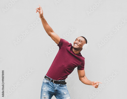 cool African american man enjoying music with headphones and dancing by gray background