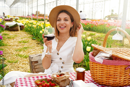 Attractive young woman having appetizer among tulip flowers. Fresh harvest with picnic and red wine in coutryside on spring time.