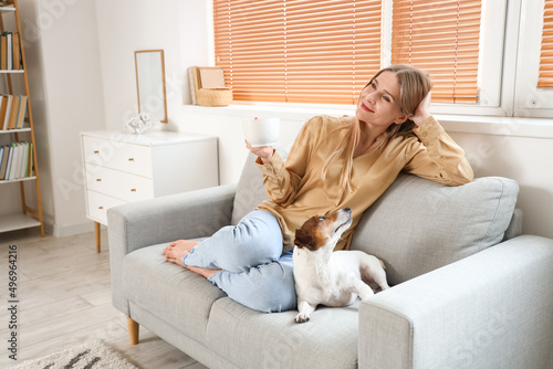 Young woman with cup of tea and Jack Russel terrier sitting on grey sofa at home