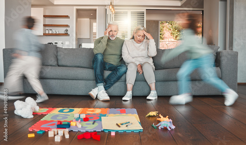 Were getting too old for this. Shot of two grandparents looking tired while their grandchildren run around at home.