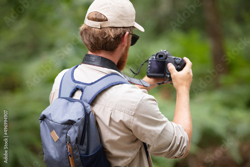 rear view of male backpacker using camera in rural setting