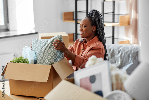 moving, people and real estate concept - happy smiling woman unpacking boxes sitting on sofa at new home