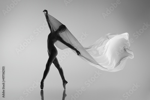 Black and white portrait of graceful ballerina dancing with fabric, cloth isolated on grey studio background. Grace, art, beauty concept. Weightless, flexible.