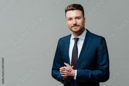 Serious male entrepreneur keeps hands together wears formal clothes dressed in office attire poses against grey background