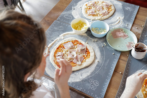 Dziecko robiące domową pizzę z serem, szynką i pieczarkami