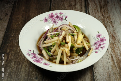 Traditional fresh lotus root or stem salad mixed with fish pickled sauce and shallot serving on the plate. Famous street food menu in Thailand. 