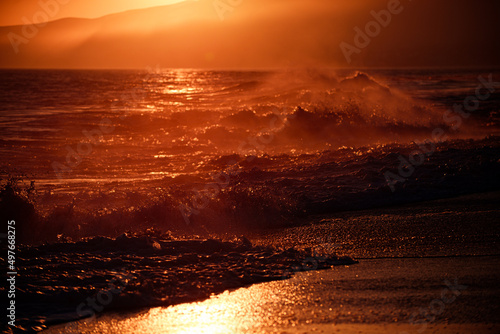 Beach sunrise over the tropical sea. Colorful sunset with wave splashes on the beach.
