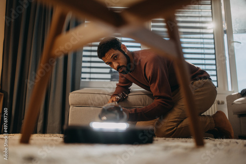 Young man hoovering carpet with vacuum cleaner in living room