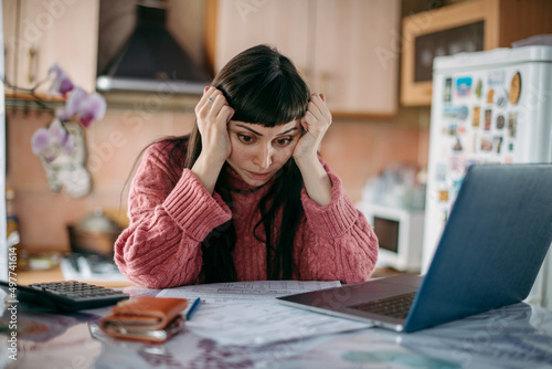 Sad woman holding her head over utility bills in front of a laptop. The concept of rising prices for heating, gas, electricity.