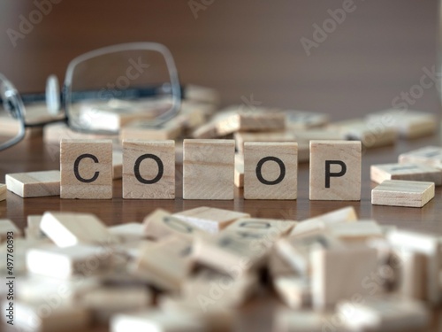 the acronym co op for copperative word or concept represented by wooden letter tiles on a wooden table with glasses and a book