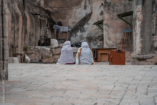 Two religious Ethiopian women in white headscarves sit on a stone step in the old city of Jerusalem. Next to them is a suitcase (1282)