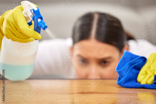 Make sure to be thorough. Shot of a young woman spraying cleaner on her coffee table.