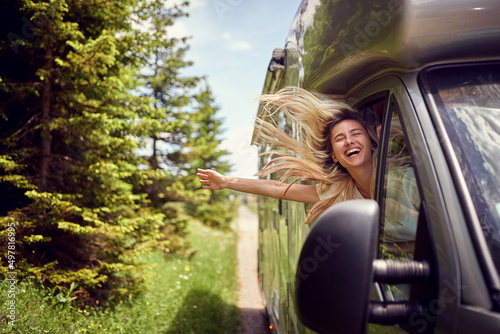 Blonde woman on the window of an rv with hands out smiling enjoying ride. Vacation time. Transport, roadtrip, nature concept.