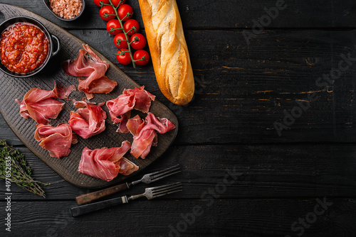 Slices of prosciutto di parma or jamon serrano set, on black wooden background, top view flat lay, with copy space for text