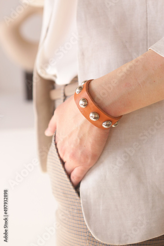 leather studded orange bracelet on woman hand closeup photo on white wall background