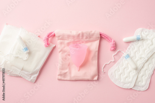 Top view photo of pink period pad bag menstrual cup sanitary napkins and tampons on isolated pastel pink background. Uterus and ovaries concept