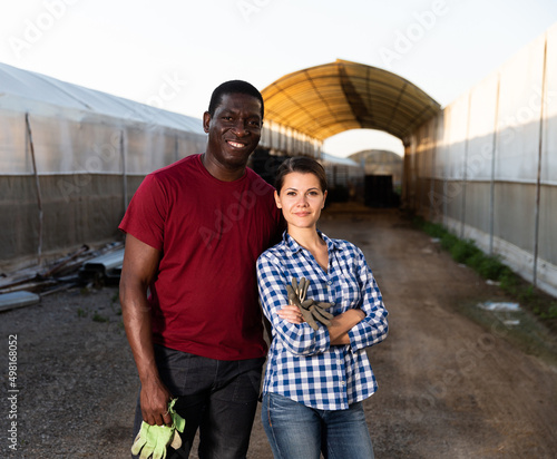 Portrait of successful confident biracial farmer couple standing outdoors on background of greenhouses