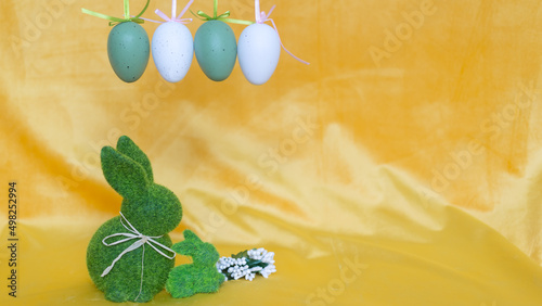 Dekoracje na wielkanoc, zielone zajączki i nakrapiane, wiszące jajka, pisanki na żółtym tle