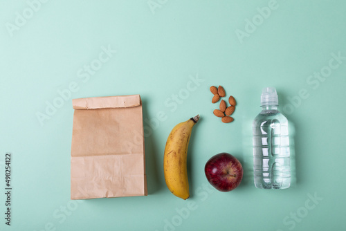 Directly above shot of paper lunch bag with fruits, almonds and water bottle on green background
