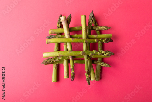 Overhead view of fresh green asparagus stacked on pink background amidst copy space
