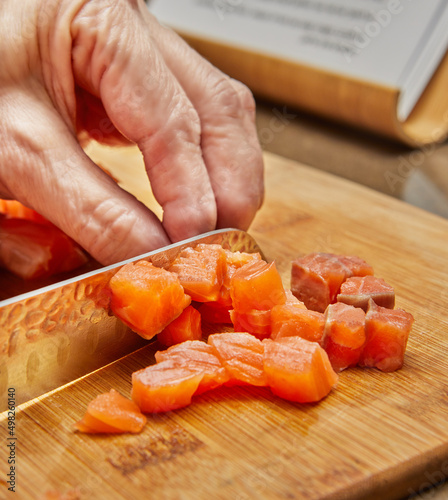 Chef cuts the salmon into cubes with knife to prepare the dish according to the recipe