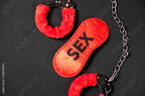 BDSM, bondage play, fetish wear and kinky sex toy concept with close up on erotic mask and red handcuffs isolated on black silk background